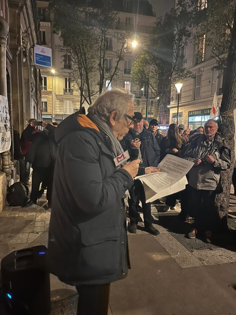 Photo d'Albert Herszkowicz devant le gymnase Japy, avec un foule sur le côté. Il tient un micro et des feuilles de papier pour tenir un discours. 